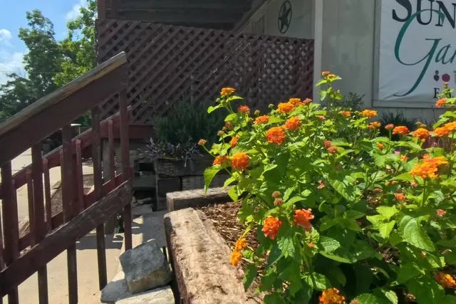 A stair rail, lantana, stonework, and the Sunken Gardens sign near a garden entry path.