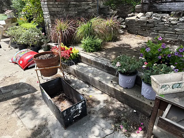 Potted flowers, planter boxes, and supplies staged near stone steps.