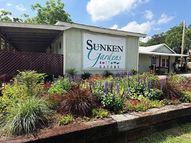The Sunken Gardens Eatery sign behind a bright front flower border with grasses and summer color.