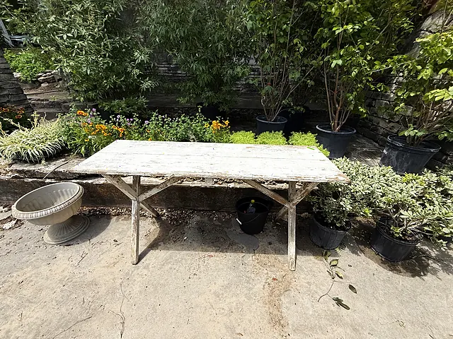 A white worktable in a shaded garden area with plants and containers nearby.