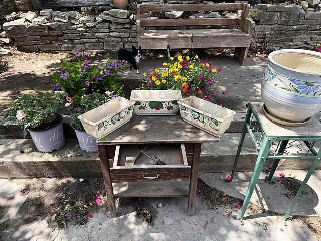 Painted rectangular planters, a ceramic pot, and flowers around a wood bench.