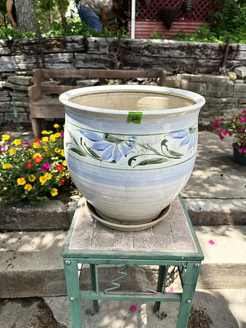 A painted ceramic planter on a green stand near stone steps and colorful flowers.