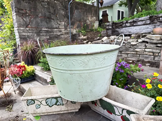 A pale tub-style planter resting inside painted rectangular planters by the stone steps.
