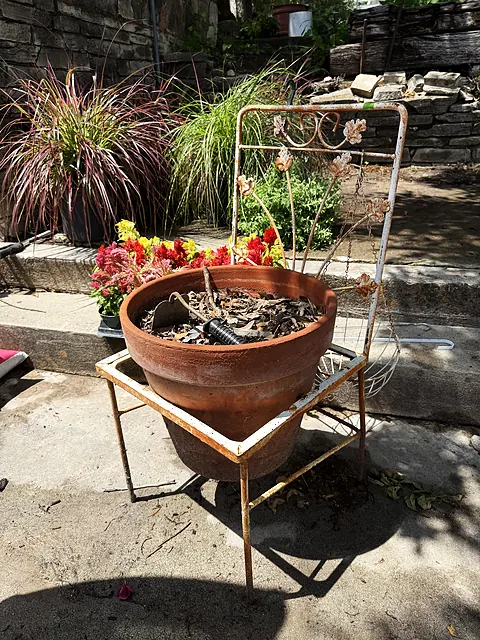 A patio planter with a trellis, leaves, flowers, and stonework behind it.