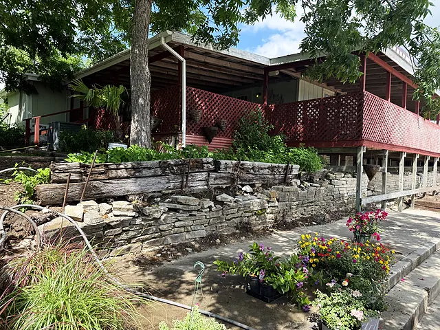 A porch terrace with stonework, red lattice, potted plants, and setup supplies.