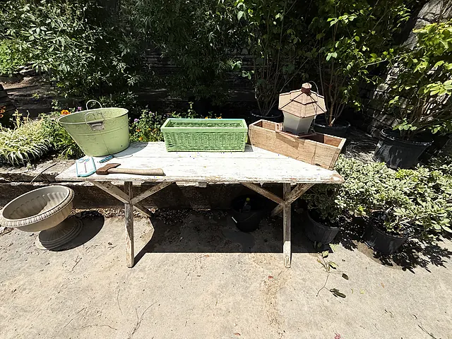 A shaded worktable with containers and plants staged around it.