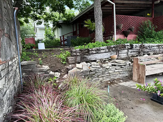 A shaded walkway with red lattice, stone edging, and nursery display setup in progress.