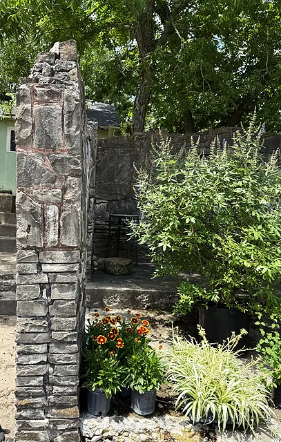 An old stone column, shade trees, and potted plants staged near the nursery entry.
