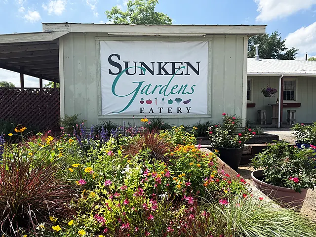 A full front-garden view of the Sunken Gardens Eatery sign with colorful planting beds.