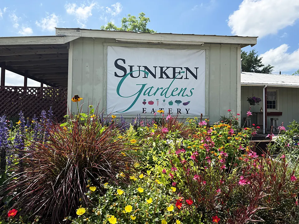 The Sunken Gardens Eatery banner on the historic building with colorful flowers in front.